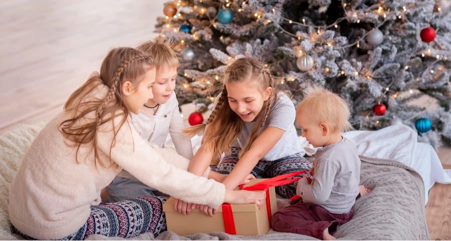 Kids opening a present in the living room near a Christmas tree.